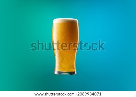Cold drops running down the glass. One full glass of frothy light beer isolated over gradient blue and green color background in neon. Concept of alcohol, drinks, holidays and festivals. Copy space Royalty-Free Stock Photo #2089934071