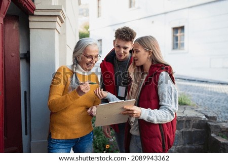 Young door to door volunteers talking to senior woman and taking survey at her front door.