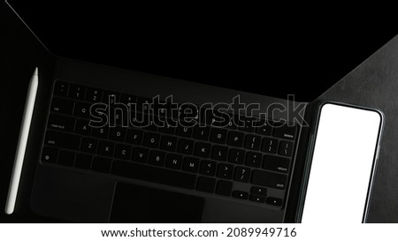 Close-up, top view of a modern black tablet or touchpad computer with smartphone blank screen on a desk.