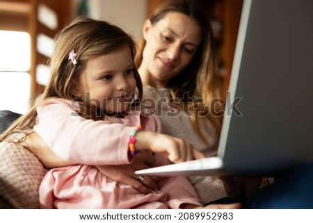 Cheerful little girl using laptop. Beautiful girl watching cartoon with mom