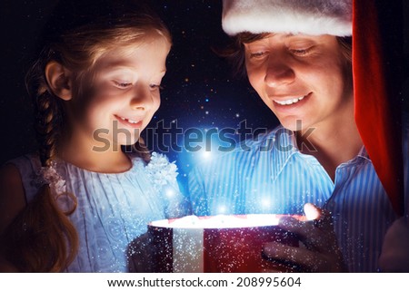 father in Santa Claus cap and daughter opened a box with Christmas gift boxes of shining light and magic
