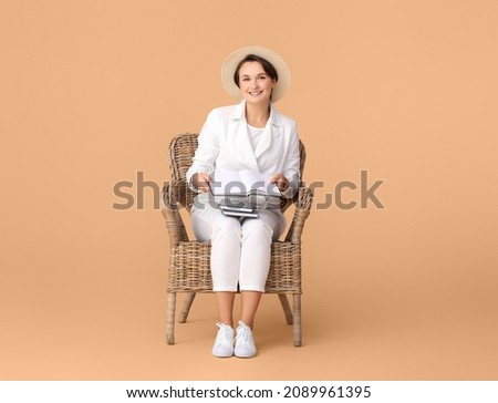 Beautiful young woman with books sitting in armchair on color background