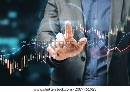 Close up of businessman hand pointing at glowing forex chart trading interface on blurry blue bokeh background. Market, economy and data exchange concept. Double exposure
