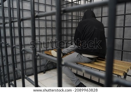 A hooded detainee is sitting in a closed temporary detention cell. Royalty-Free Stock Photo #2089963828