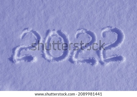 The inscription on the white snow surface is 2022. Symbol of the next year marked against a snowy winter background. Color of the year 2022. Ultra Violet creative and moody color of the picture