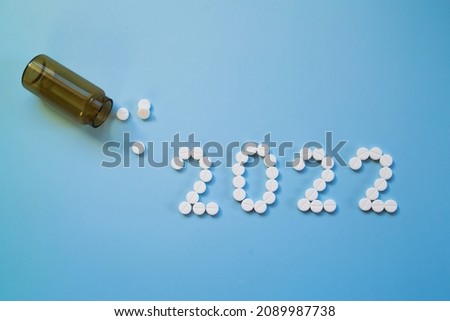 White medical pills and tablets spilling out of a drug bottle on a blue background. Christmas theme, pills like a Christmas tree. So boxes as an arrow copy space.