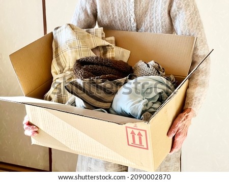 Hands of an elderly woman holding a cardboard box containing clothes Royalty-Free Stock Photo #2090002870