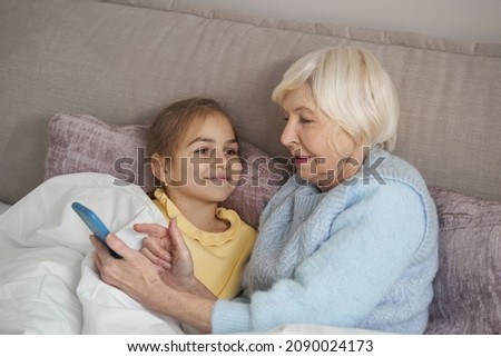 Focused elderly lady exploring smartphone menu with little girl