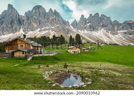 Majestic spring alpine landscape, wooden houses on the green fields and small lake with mountains in background, Geisler - Odle mountain group, Alto Adige, Dolomites, Italy, Europe Royalty-Free Stock Photo #2090033962