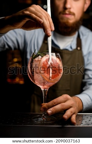 Front view of goblet glass with cold cocktail that the hand of barman neatly decorating by a slice of grapefruit using tweezers Royalty-Free Stock Photo #2090037163