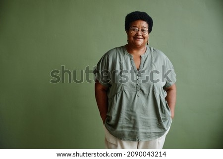 Waist up portrait of black senior woman smiling at camera while standing against green background, copy space Royalty-Free Stock Photo #2090043214