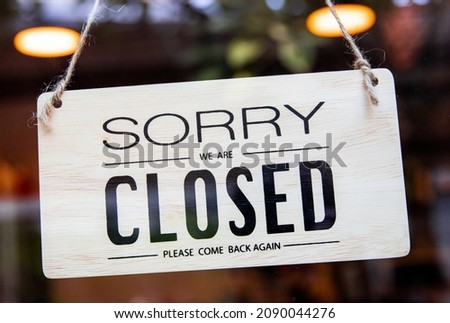 Wooden closed signage hanging on the glass wondow and door for covid-19 lockdown on the blurred background.