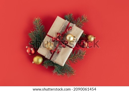 Craft gift box with spruce branch and christmas ornaments on a red background. Holiday concept. Place for text. Flat lay.