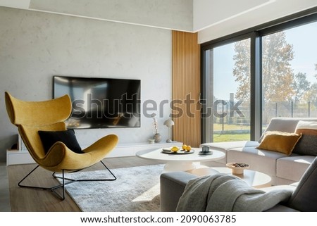 Modern living room interior design with corner beige sofa, creative rounded coffee tables, mustard armchair and personal accessories. Panoramic windows. Template. 