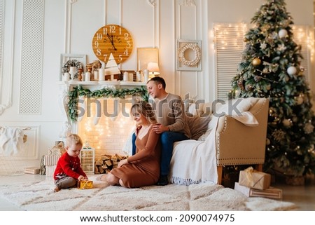 mom and dad give box with gift to little son by fireplace in room decorated for the new year. the tradition of making gifts for the new year. a child's faith in Santa Claus and a miracle. toy store.
