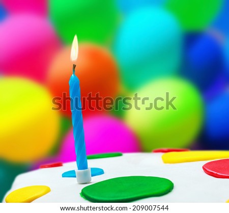 Lighted candles on a birthday cake on the background of balloons