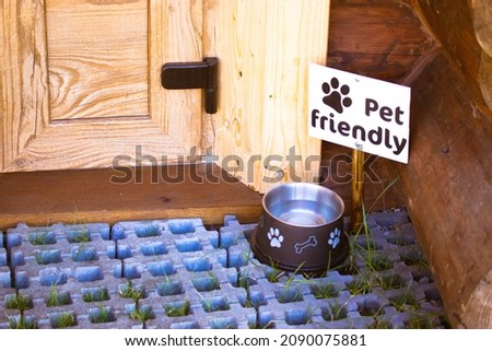 Pet friendly sign. A dog's paw picture on a sign standing outside by a door near the alluminium water bowl to quench a pet's thirst. Dogs welcome cafe. Canine animal theme. Cat food utensils outdoors.