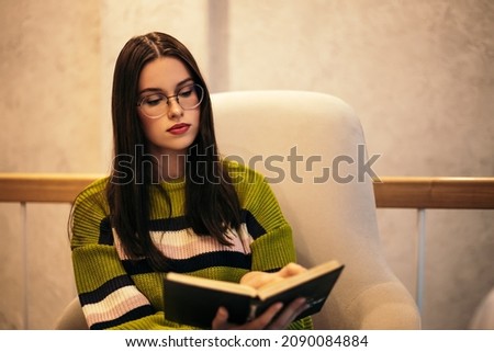 Woman sitting cafe or restaurant reading book while waiting for order. Relaxing after hard working day. Student doing homework, distance learning. Lady wear glasses spend her free time profitably
