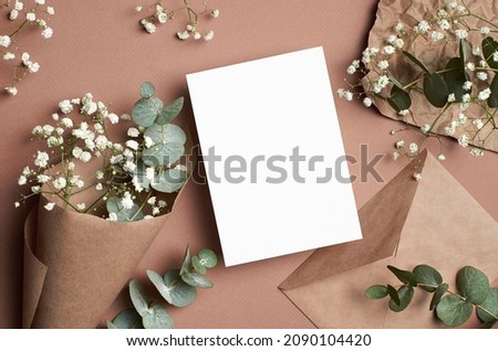 Wedding invitation or greeting card mockup with envelope, eucalyptus and gypsophila flowers on beige paper background
