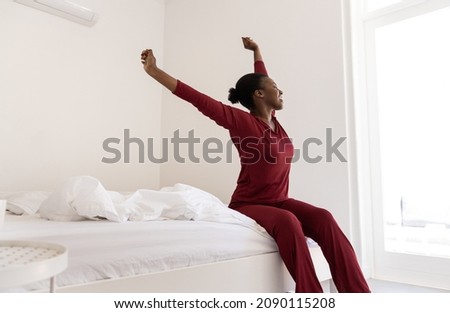 Early morning routine of beautiful Black African Woman stretching arms outwards while sitting on bed, with copy space Royalty-Free Stock Photo #2090115208