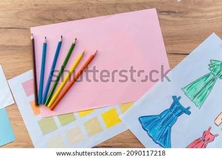 Creating new fashion collection background. Hand drawn sketches of clothes and color swatches on wooden table, top view. Creativity, dressmaking and design concept 