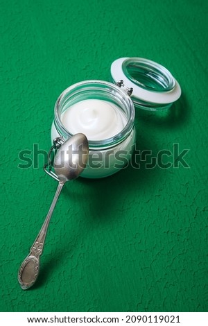 homemade yogurt in a glass jar and spoon on a green textured background