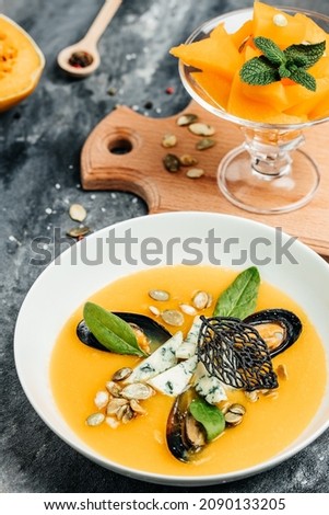 Pumpkin traditional soup with eafood, mussels, shrimps, blue cheese, mold in a white bowl. vertical image. top view.