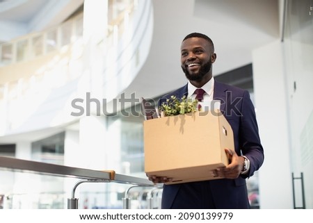 Happy young black man in suit got new job, walking by modern office, holding box with his belongings, looking at copy space and smiling. Job opportunity, career for millennials concept Royalty-Free Stock Photo #2090139979