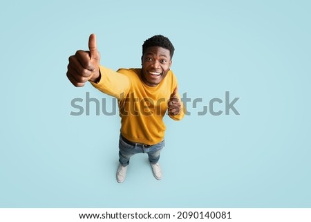 Top view of joyful handsome african american millennial guy in nice outfit showing thumb up and smiling at camera on blue studio background, recommending something exciting, copy space, full length Royalty-Free Stock Photo #2090140081