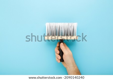 Young adult man hand holding new brush on light blue table background. Pastel color. Closeup. Preparation for repair work of home.
