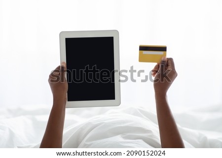 Cropped of black woman holding modern digital tabllet with empty screen and credit card, unrecognizable african american lady shopping online while chilling in bed at home, closeup photo