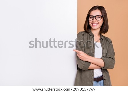Photo of cheerful lady direct forefinger placard board empty space wear specs khaki shirt isolated beige color background Royalty-Free Stock Photo #2090157769