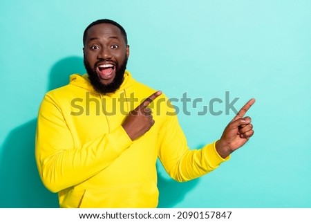 Photo of brunette impressed millennial beard guy indicate empty space wear yellow sweatshirt isolated on teal color background
