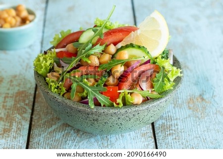 Healthy Vegetarian Chickpea Salad in a bowl with vegetables, herbs and dressing on a blue wooden background. Healthy food concept. Royalty-Free Stock Photo #2090166490