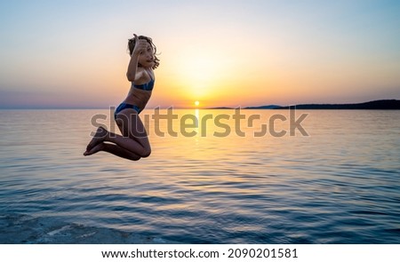 Girl jumping from pier in the water at sunset holding thumbs up sign. Child jumping in the sea in Silba, Croatia.