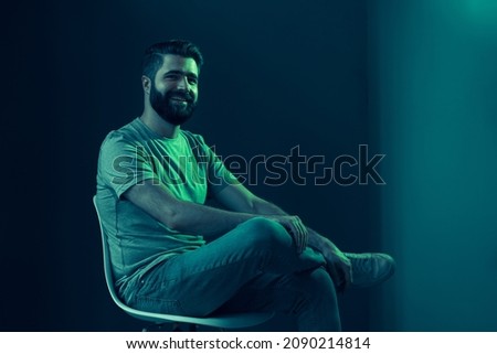 Neon portrait of a young attractive man in the studio. The guy sits on a stylish white chair