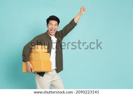 Asian man holding package parcel box and hands up raised arms isolated on green background, Delivery courier and shipping service concept Royalty-Free Stock Photo #2090223145