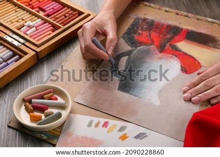 Woman drawing beautiful jug with soft pastel at wooden table, closeup