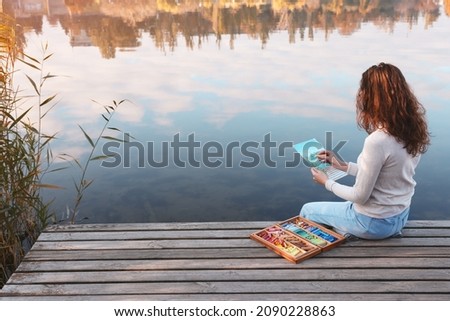 Woman drawing with soft pastels on wooden pier near water