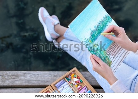 Woman drawing with soft pastels on wooden pier near river, closeup