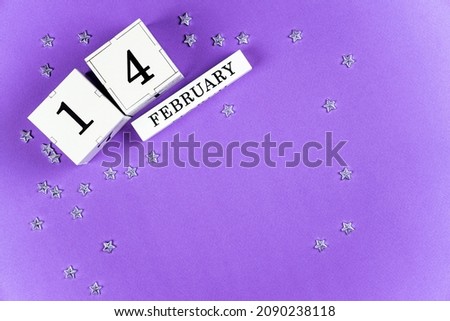 Valentine's Day purple, lilac trendy background perpetual calendar white block with the date February 14, a scattering of silver stars. Copy space, flatlay.