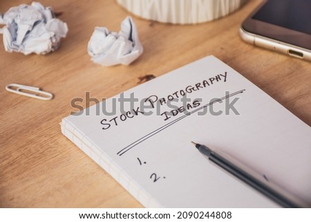 Handwritten text stock photography ideas on notepad on wooden desk background. 