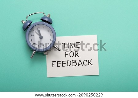 blue alarm clock lies on a blue background next to a card with the text time for feedback. Conceptual business photo on the topic of product evaluation and customer reviews.