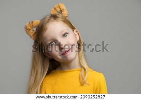 Cute smiling blond girl with tiger ears. A headdress with tiger ears. New Year 2022. Child in a tiger costume smiles sweetly and looks at camera.