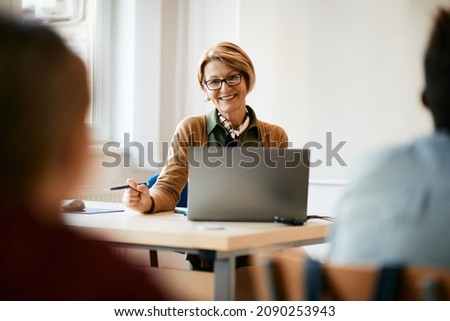 Happy mature teacher giving lecture to her elementary students and using laptop during a class.
 Royalty-Free Stock Photo #2090253943