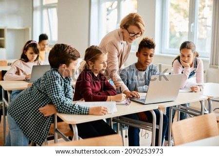 Elementary teacher and her students using laptop during computer class at school. Royalty-Free Stock Photo #2090253973