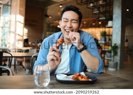 Happy  Asian man eating BBQ chicken wings in restaurant. Royalty-Free Stock Photo #2090259262