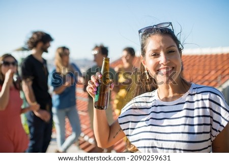 Portrait of smiling woman with dark hair at party. Young girl in striped T-shirt looking at camera. Friends of different nationalities in background. Party, friendship concept
