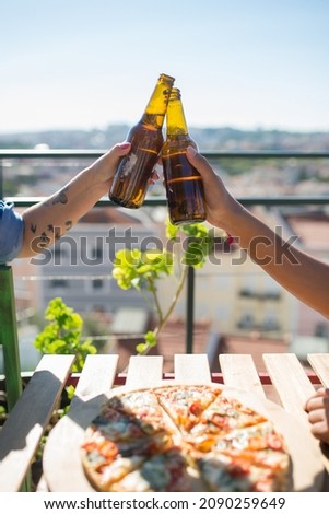 Close-up of friends clinking beer bottles. Male and female hands holding bottles over table with pizza. Party, friendship concept