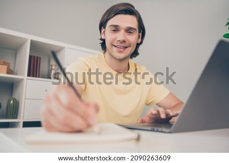 Photo of cheerful nice university student guy sit desk pc write copybook wear yellow t-shirt home indoors